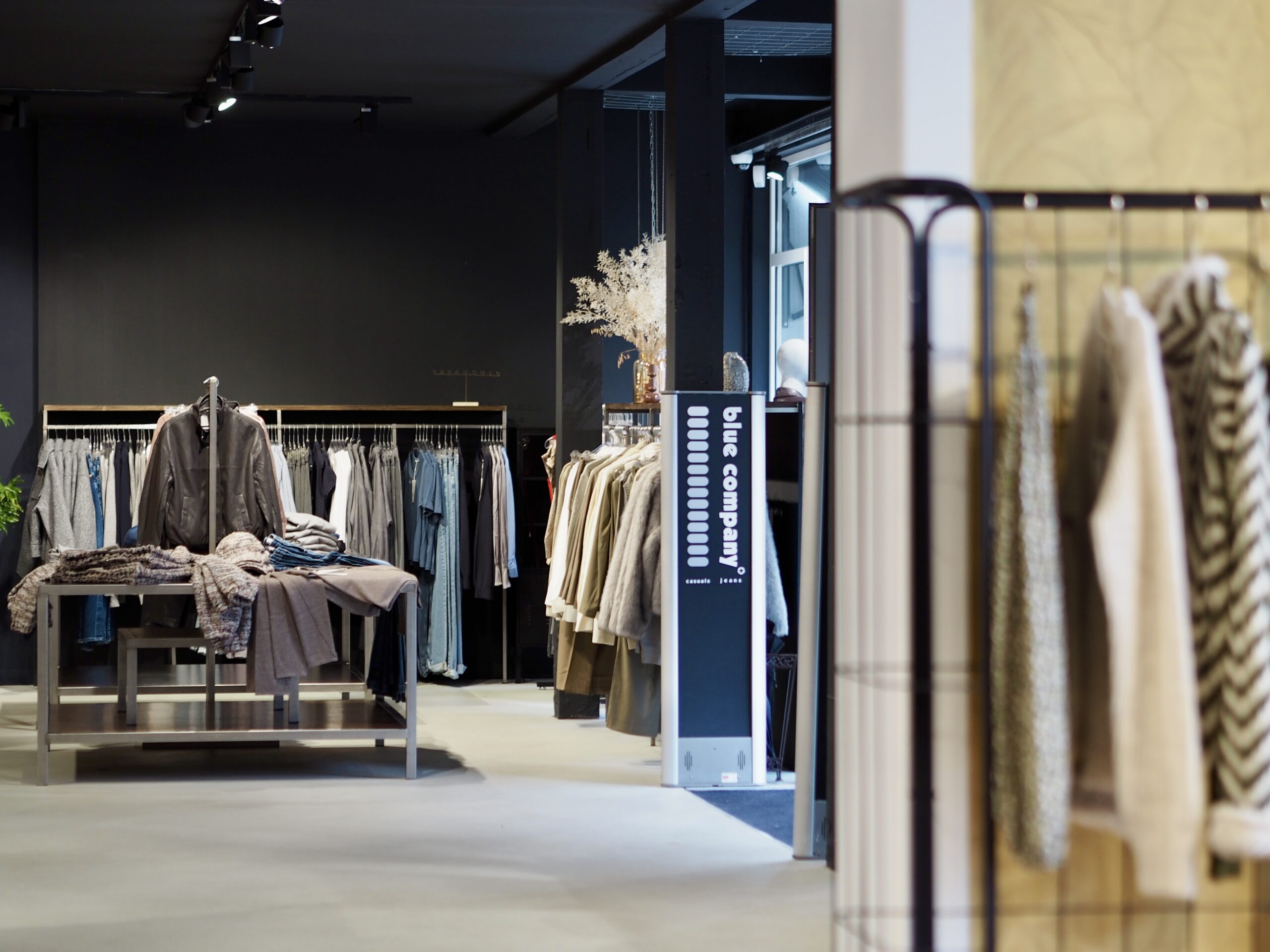 Gemütliche Boutique mit Schaufensterpuppen am Fenster, einem goldenen Kunstwerk an der Wand und mehreren Kleiderständern; Duftmarketing schafft ein angenehmes Einkaufserlebnis.